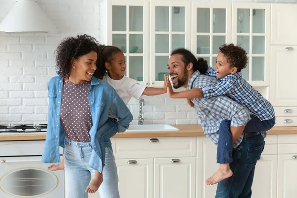 Feliz pais afro-americanos porquinho apoiando crianças na cozinha — Fotografia de Stock