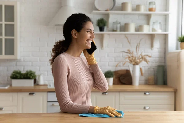 Happy housewife clean kitchen desk talking on cell