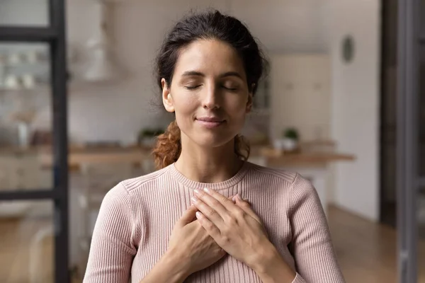 Calma giovane donna si tiene per mano sul petto pregando — Foto Stock