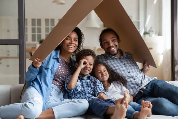 Heureuse famille afro-américaine assise sur le canapé sous le toit en carton — Photo