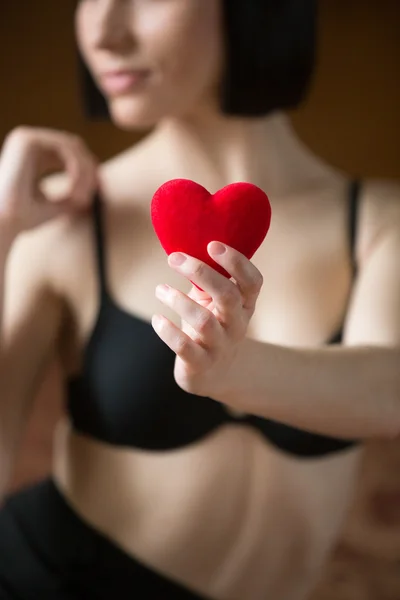 Ragazza sexy in reggiseno nero tiene il cuore rosso per San Valentino — Foto Stock