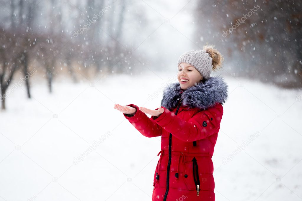 Happy smiling female in red winter jacket catching the snow with