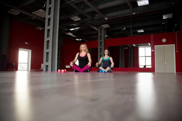 Duas meninas bonitas sentam-se de pernas cruzadas em tapetes no centro de fitness — Fotografia de Stock