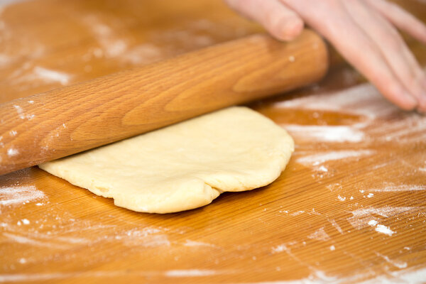 Woman's hands roll dough on the table