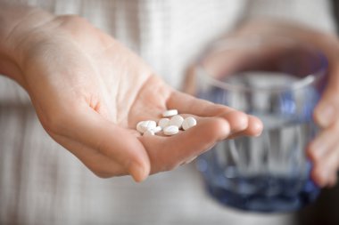 Womans hands holding heap of white round pills and glass of wate clipart