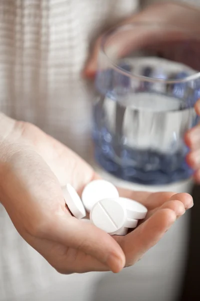 Manciata di pillole rotonde bianche e bicchiere d'acqua nelle mani delle donne — Foto Stock