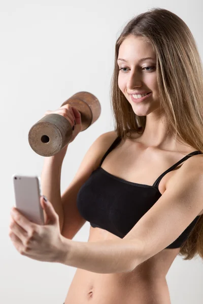 Dumbbell tutarak ve selfie zeki ile alarak gülümseyen sportif kız — Stok fotoğraf
