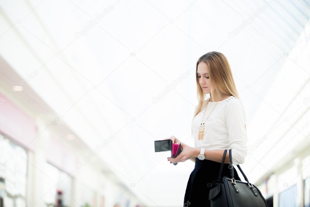 Young female standing with opened wallet in shopping mall