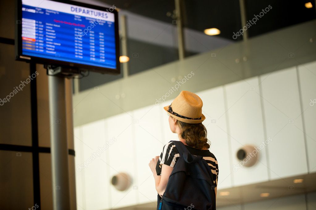 Woman in front of airport flight information panel 