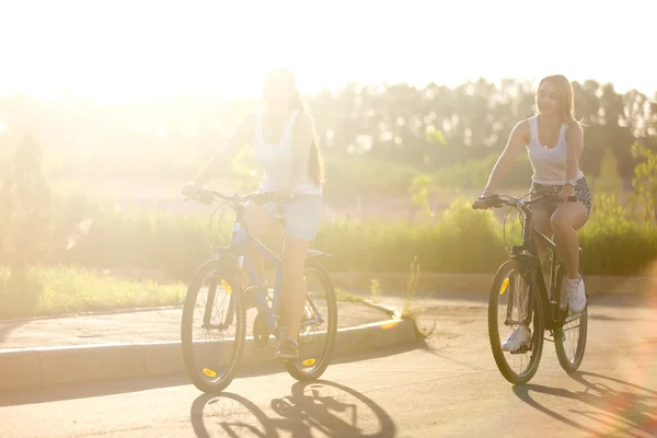Duas jovens mulheres em passeio de bicicleta à luz do sol — Fotografia de Stock