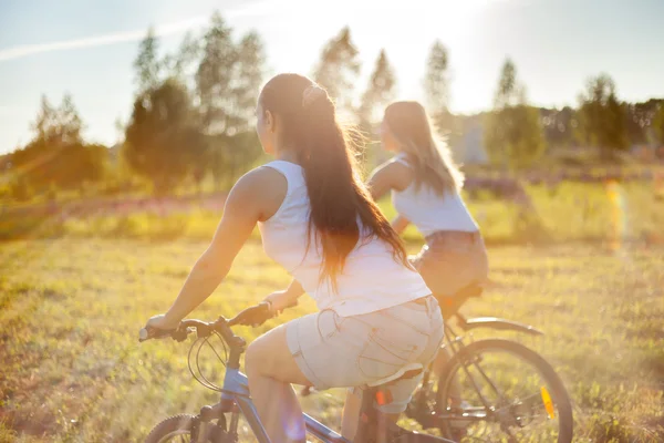 Jovens amigas andando de bicicleta à luz do sol — Fotografia de Stock