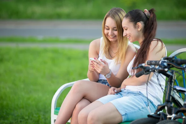 Cheerful teenage girls playing with cellphone on bench — Stockfoto