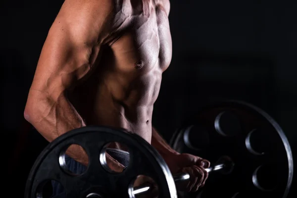 Muscular man lifting a barbell in fitness center — Stok fotoğraf