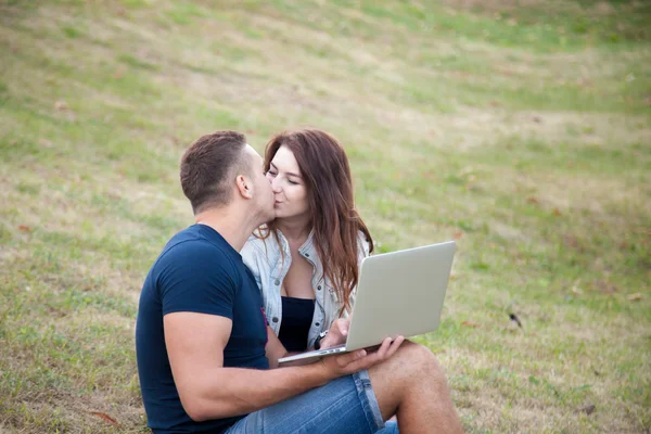 Couple with laptop kissing in park — Stock fotografie
