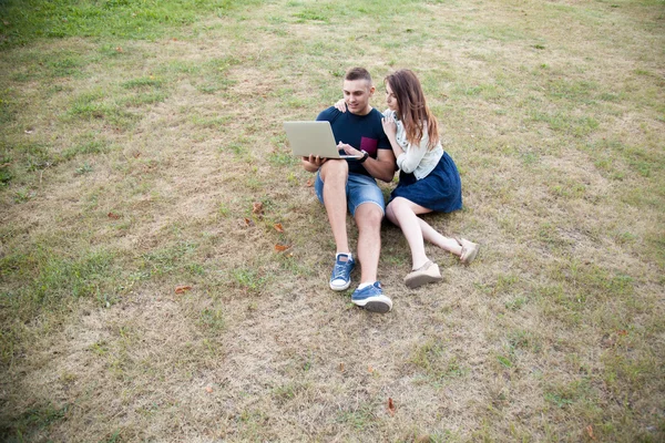 Coppia seduta con computer portatile su erba — Foto Stock