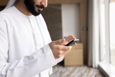 Smartphone applications. Close up young Arab male in traditional Islamic wear using phone. Muslim office worker employee executive student communicate online text message on cell concept. Copy space