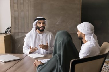 Pros and cons. Professional confident Islamic bank manager financial adviser consult young Muslim couple convince to sign investment agreement recommend life insurance program help with tax planning