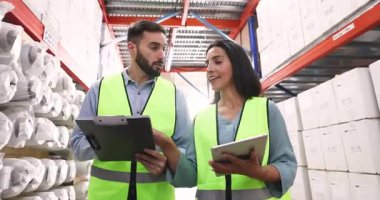 Two warehouse workers wearing safety vests walking along aisle in storehouse holding clipboard and tablet, finalize meeting with handshake, gesture of trust, agreement, effective teamwork conclusion