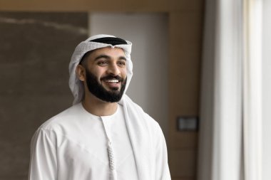 Confidence and motivation. Smiling ambitious young Arab male in traditional Islamic white thobe student businessman company leader stand in office feel proud of success in career education. Copy space