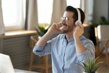 Happy listener. Cheerful inspired young businessman in modern headphones look aside from notebook pc screen with smile take break in work to relax by pleasant music enjoy audio podcast relieve stress