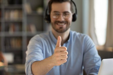 Confidence and quality in customer support. Blurred workplace portrait smiling young telemarketer helpdesk operator in headset show thumbs up to camera. Perfect service consultation guarantee concept