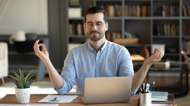 Office zen. Calm young businessman corporate worker remote employee meditate at workplace with closed eyes practice relaxation yoga breathing before notebook recharge mental energy boost productivity