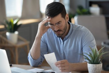 Financial stress. Concerned worried young businessman accountant entrepreneur analyze payments at office desk read bank document troubled by overdue bill unexpected debt penalty fee budget overrunning