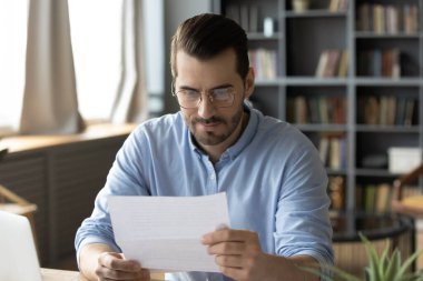 Professional correspondence. Smart young businessman lawyer read paper document received by mail at office desk engaged in legal review of contract terms conditions analyze contractor official answer