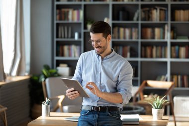 Elearning and research. Smiling motivated young businessman student using digital tablet device in office or library engaged in browsing information study materials manage scientific project online