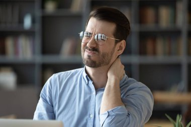 Office fatigue. Head shot portrait tired overworked young adult man grimace with pain suffer from sore neck muscle tension after uncomfortable work posture long sitting at computer unhealthy lifestyle