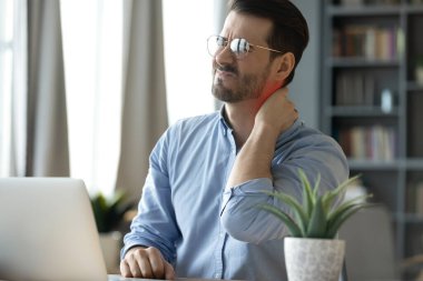 Too much sedentary work. Stressed exhausted millennial businessman office worker sit at desk by pc rub back of neck show painful reaction chronic fatigue syndrome body strain caused by poor posture