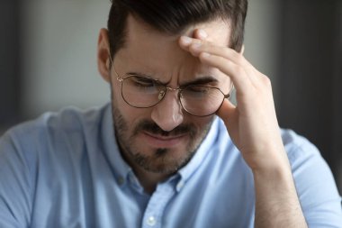 Nervous tension. Close up sad upset millennial businessman in glasses sit with eyes closed touch forehead deep in heavy thoughts suffering from headache migraine burnout fatigue information overload