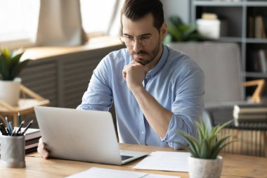 Focused analysis. Busy pensive mid adult man office worker sit at desk by notebook screen read finance report engaged in electronic paperwork consider project strategy think over work problem solution