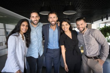 İş ekibinin birliği iş yerinde. Çeşitli çok ırklı gülümseyen şirket çalışanları grup halinde fotoğraf çektirmek için toplanıyor. Kameraya bakıyor, takım çalışmasının ruhunu yansıtıyor.