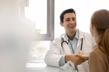 Üniformalı mutlu erkek terapist pratisyen doktor, klinik muayene odasında kadın hastalarla görüşüyor, gülümsüyor, masada oturuyor. Sağlık hizmetleri, sağlık sigortası, sağlık haberleri