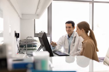 Gülümseyen doktor tanısal test sonuçlarını açıklıyor, dijital röntgen ya da laboratuvar sonuçlarını gösteren pc ekranına işaret ediyor, kadın hastalara olası tedavi seçenekleri ve önleyici bakımda rehberlik ediyor