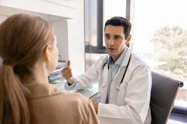 Modern klinikteki kadın hastaya danışmanlık yaparken palto giyen erkek doktor konuşuyor, tıbbi danışma, güvenilir iletişim, tedavi planıyla ilgili önde gelen sağlık hizmetleri tartışmaları