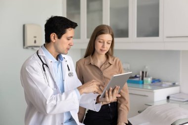 Erkek doktor, klinikte dijital tablet kullanan genç kadın hastaya tıbbi bilgileri, tomografi görüntüleme sonuçlarını, tedavi planını paylaşmayı, yeni teletıp platformunu veya uygulamasını tartışmayı açıklıyor.