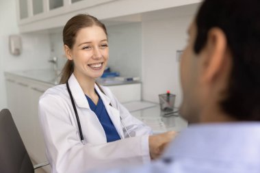 Pozitif hemşire hastayla tokalaşıyor, prosedürü başlatıyor ya da nihai hale getiriyor, kontrol ya da tanı koyuyor modern muayene odasındaki masada oturuyor, gülümsüyor, dostça bir jest yapıyor ve...