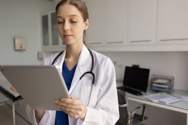 Klinikte tablet üzerinde çalışan, verilere erişen, uzaktan ilaç yazan, muayene odasında tek başına dururken teletıp uygulaması ya da platformu kullanan ciddi Arjantinli hemşire.