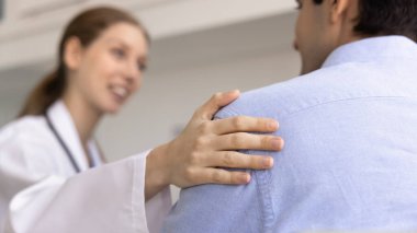 Yakın plan, şefkatli kadın doktor erkek hastaların omuzlarına nazikçe dokunarak, özel bir klinikte yapılan görüşme sırasında empati ve güvence gösteriyor. Destek, sağlık hizmetleri