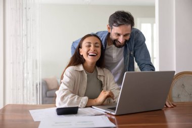 Yurt içi muhasebe sevinci. Gülen evli çift, ev işlerindeki aile finansmanını yönetirken bilgisayarla mutlu anları paylaşıyor. Hesap makinesiyle bütçe çalışması yapıyor.