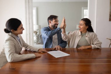 Zafer anı. Heyecanlı orta yaşlı evli çift, emlakçı emlak danışmanıyla iş anlaşması imzalandıktan sonra başarılı bir anlaşmayı kutlarken beşlik çaktı.