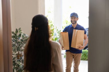 Dakik yemek siparişi servisi. Arkaya bakan bayan müşteri kapısı açık. Süpermarketten satın alınan, güler yüzlü, profesyonel teslimatçı adam tarafından internetten alınmış büyük kağıt torbaları kabul etmek için.
