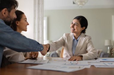Güvenini kazandığıma sevindim. Mutlu gülümseyen kadın finansal danışman profesyonel istişareden sonra çiftlerle tokalaşıyor bütçe değerlendirmelerini bitiriyor finans planlamasına yardımcı oluyor.