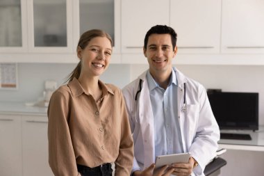 Beyaz önlüklü yakışıklı erkek doktor kameraya kadın için dijital tablet taşıyor. Hasta, profesyonel sağlık hizmetlerinden memnun. Güvenilirlik, güven, sigorta