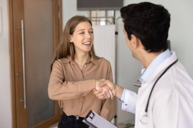 Profesyonel erkek terapist ya da beyaz üniformalı doktor elinde hafıza kaybı ya da hastalık geçmişi olan bir pano tutarak elini sıkan kadın, iyi sağlık sonuçlarıyla ya da iyileşme süreciyle hastayı tebrik ediyor