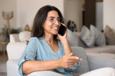 Pozitif nişanlı güzel İspanyol gözlüklü kadın evde cep telefonuyla konuşuyor, telefon görüşmesinden, cep telefonundan, iletişimden, iyi haberlerden, konuşmaktan, gülümsemekten hoşlanıyor.