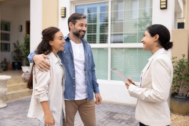Hayalimdeki evi arıyorum. Dost canlısı genç kadın emlakçı ev girişinin yanında evli müşterilerle buluş dijital tablet tut ipotek kredisi satın alma detaylarını tartış gayrimenkul nesnelerini göstermeden önce