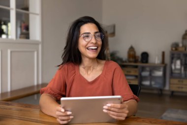 Zarif gözlüklü, tablet bilgisayarlı, iş yerindeki masada oturan, yüzünü çeviren, gülümseyen, gülen ve internet iletişiminden keyif alan genç İspanyol bağımsız kadın.